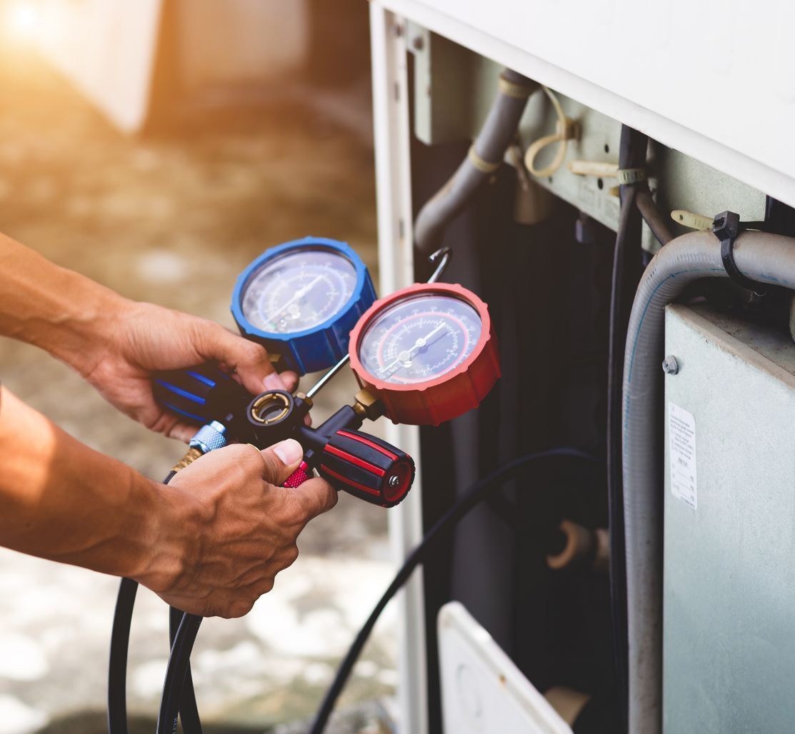 A man is working on an air conditioner with two gauges.