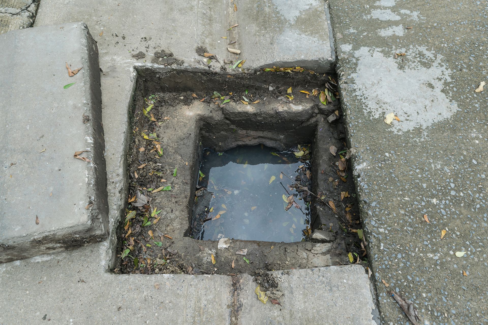 Open square drain hole in cracked concrete pavement with water inside