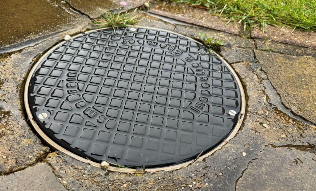 A manhole cover is sitting on a sidewalk next to a grassy area.