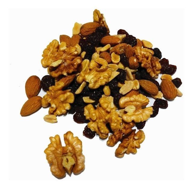 Montón de mezcla de frutos secos: nueces, almendras, maní y pasas, sobre un fondo blanco.