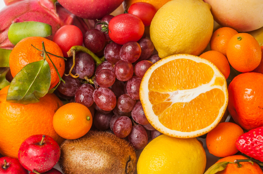 Frutas frescas variadas: media naranja, uvas, limones, mandarinas, manzanas, kiwi y bayas.