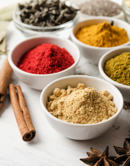 Cuencos de especias de colores: rojas, amarillas, verdes y marrones, con ramas de canela y anís estrellado.