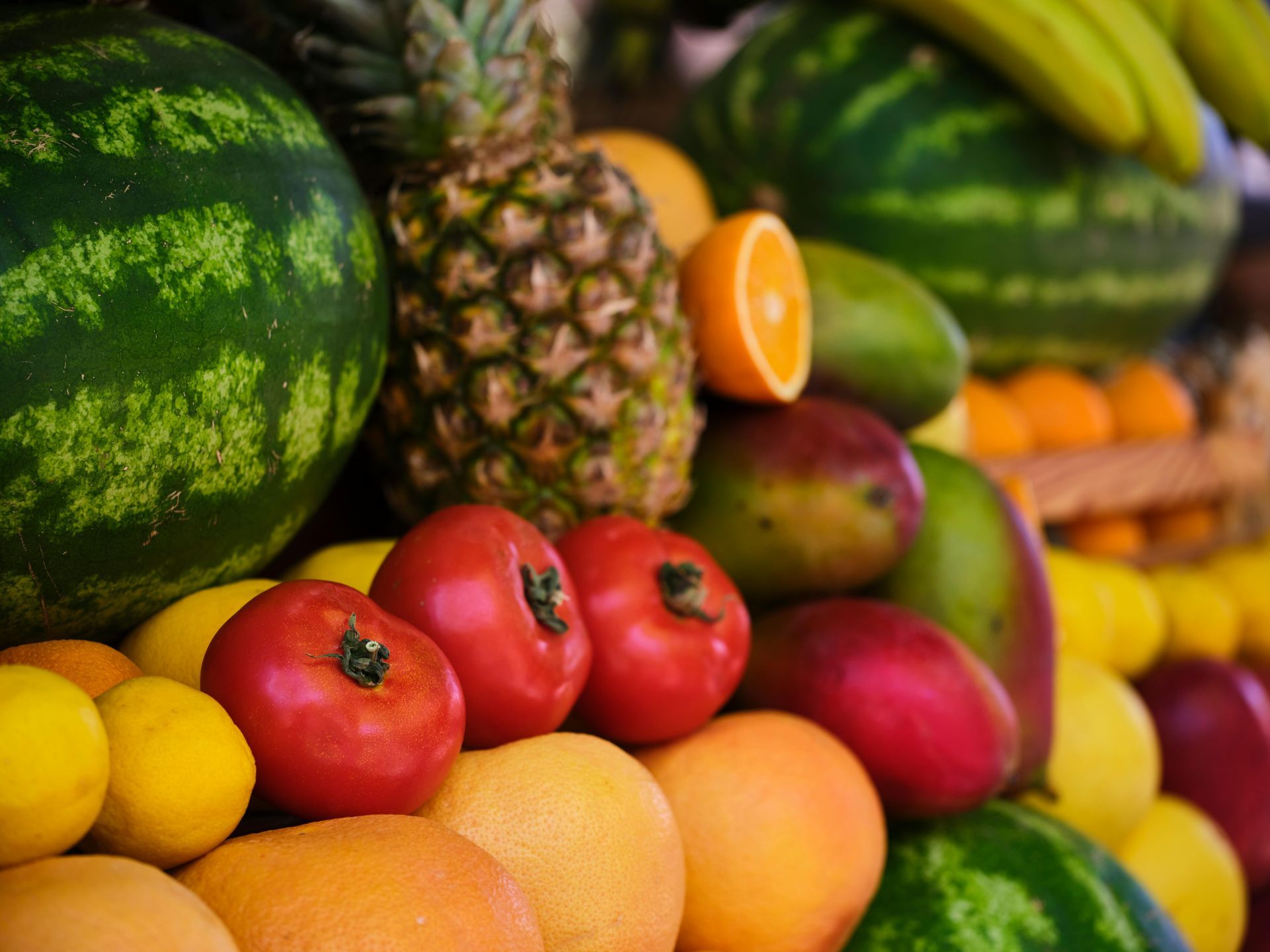 Pila de frutas frescas: sandías, piñas, naranjas, mangos, plátanos, tomates y limones.
