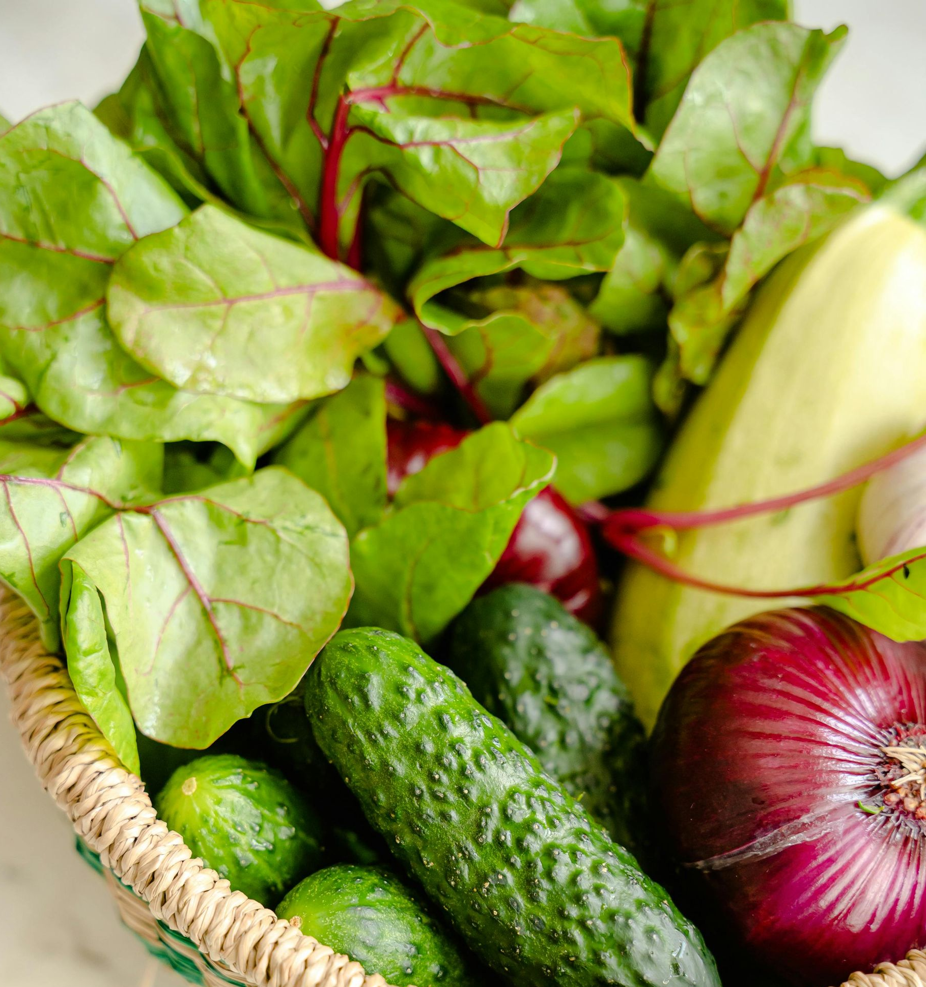 Cesta de verduras frescas: pepinos, cebolla roja, calabacín, remolacha y verduras de hoja verde.