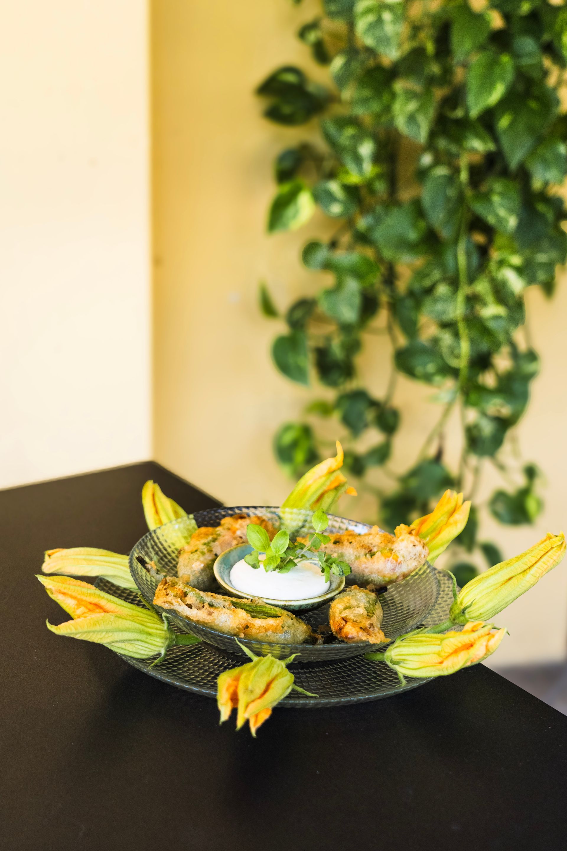 Un piatto bianco di insalata scura guarnito con verdure e fiori su un tavolo, sullo sfondo sfocato di un prato.