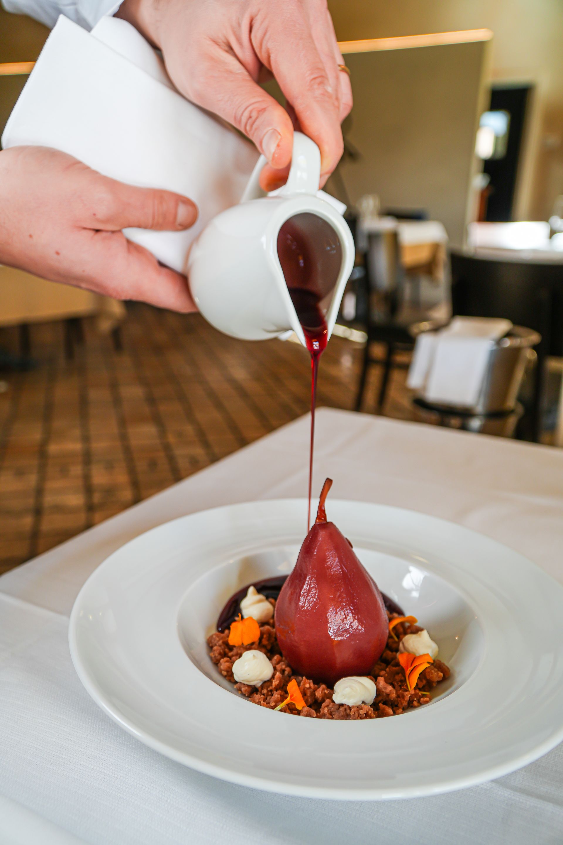 Elegante piatto gourmet impiattato con microverdure e salsa, servito a parte un bicchiere di vino bianco su un tavolo.