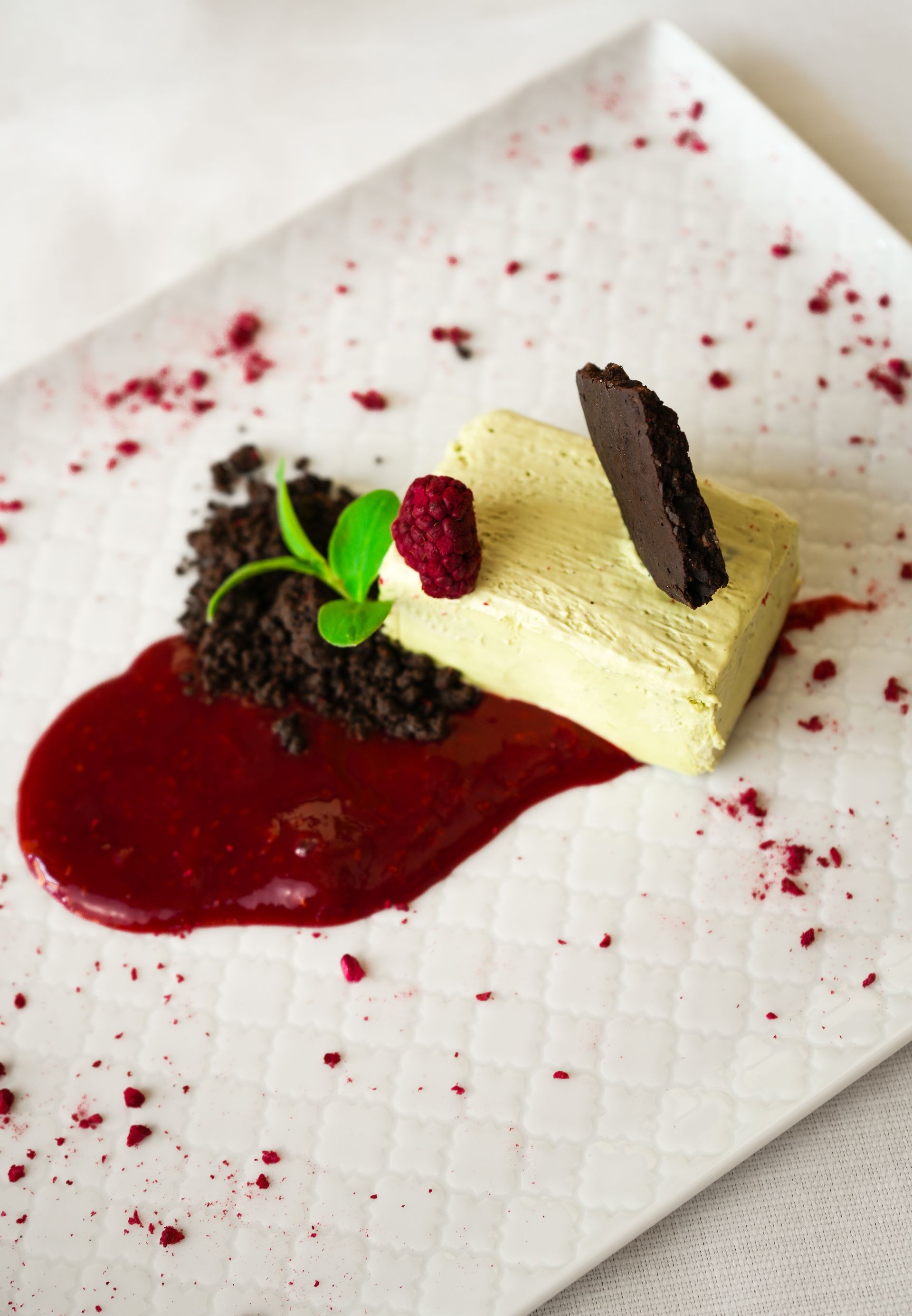 Piatto nero con bocconcini di dessert, frutta e crema spolverata di zucchero a velo su un tavolo di legno.