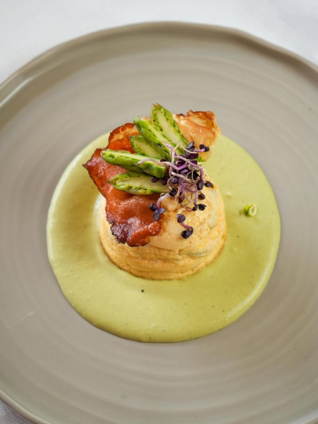Piatto gourmet impiattato con carne scottata, asparagi e guarnizione viola su salsa verde.