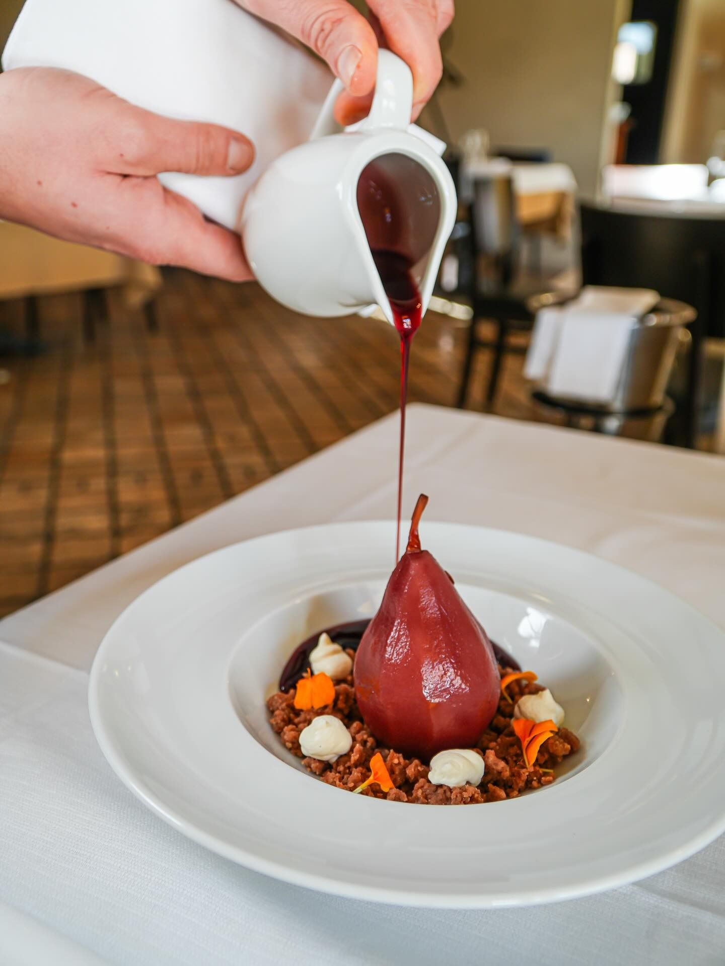 Lo chef versa della salsa rossa su un dessert servito in una ciotola bianca a un tavolo di un ristorante.
