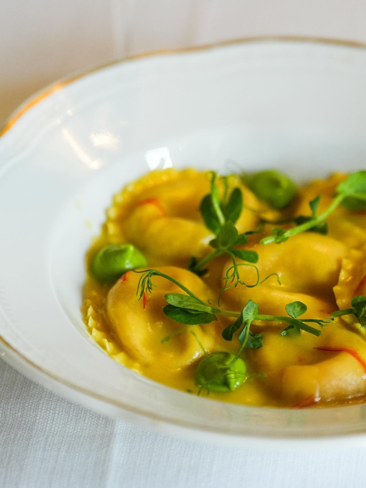 Ciotola bianca di ravioli gialli guarniti con erbe aromatiche e salsa verde