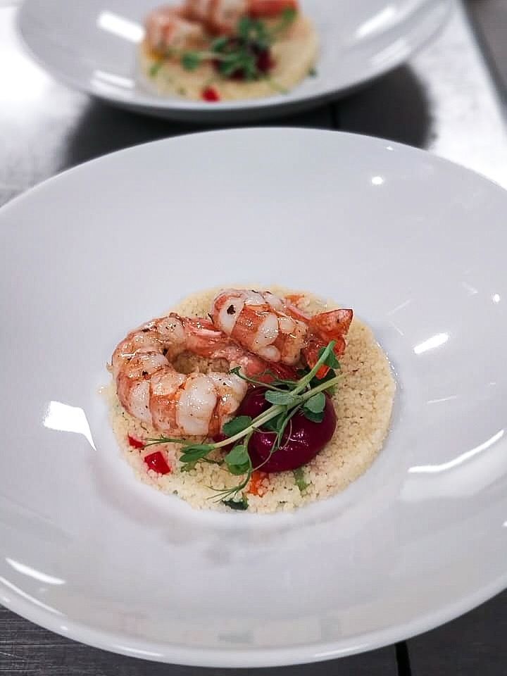 Antipasto di gamberi servito in una ciotola bianca con salsa ed erbe aromatiche, su un tavolo di ristorante.