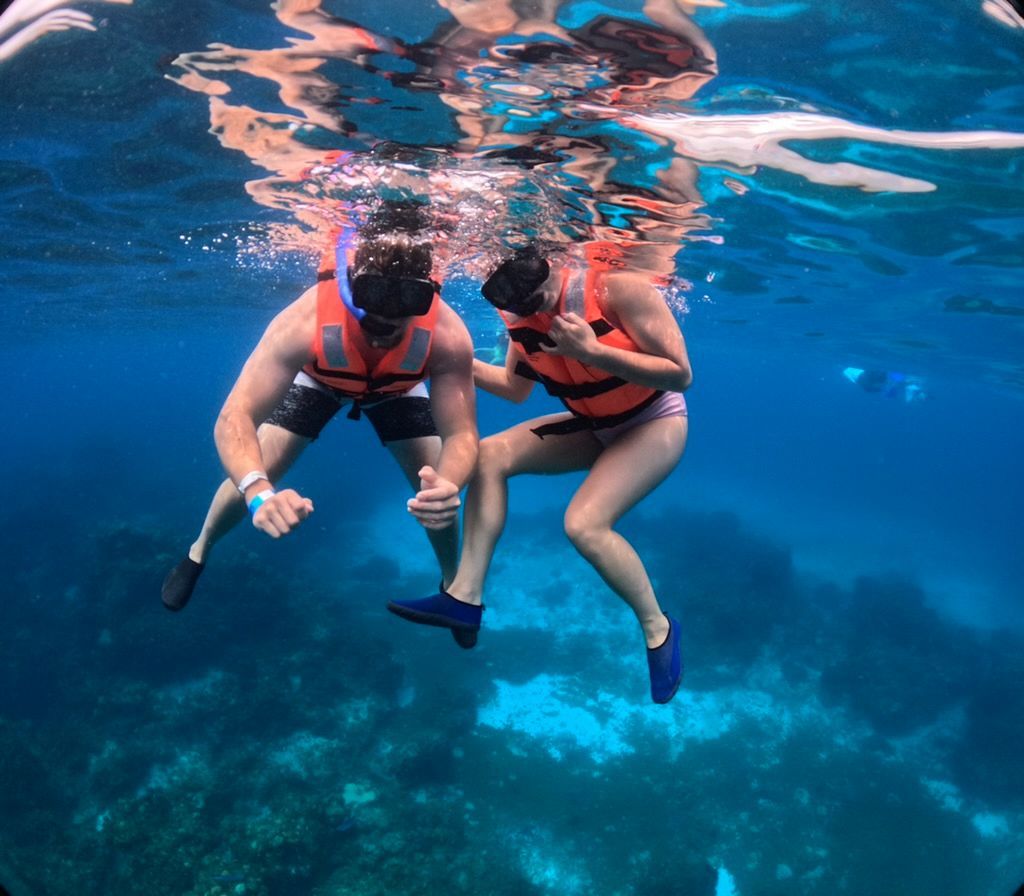 Two snorkelers in orange life vests floating underwater above a coral reef, seen from the surface.
