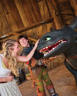 Woman and boy pet a black dragon puppet in a wooden hut, smiling as they interact.