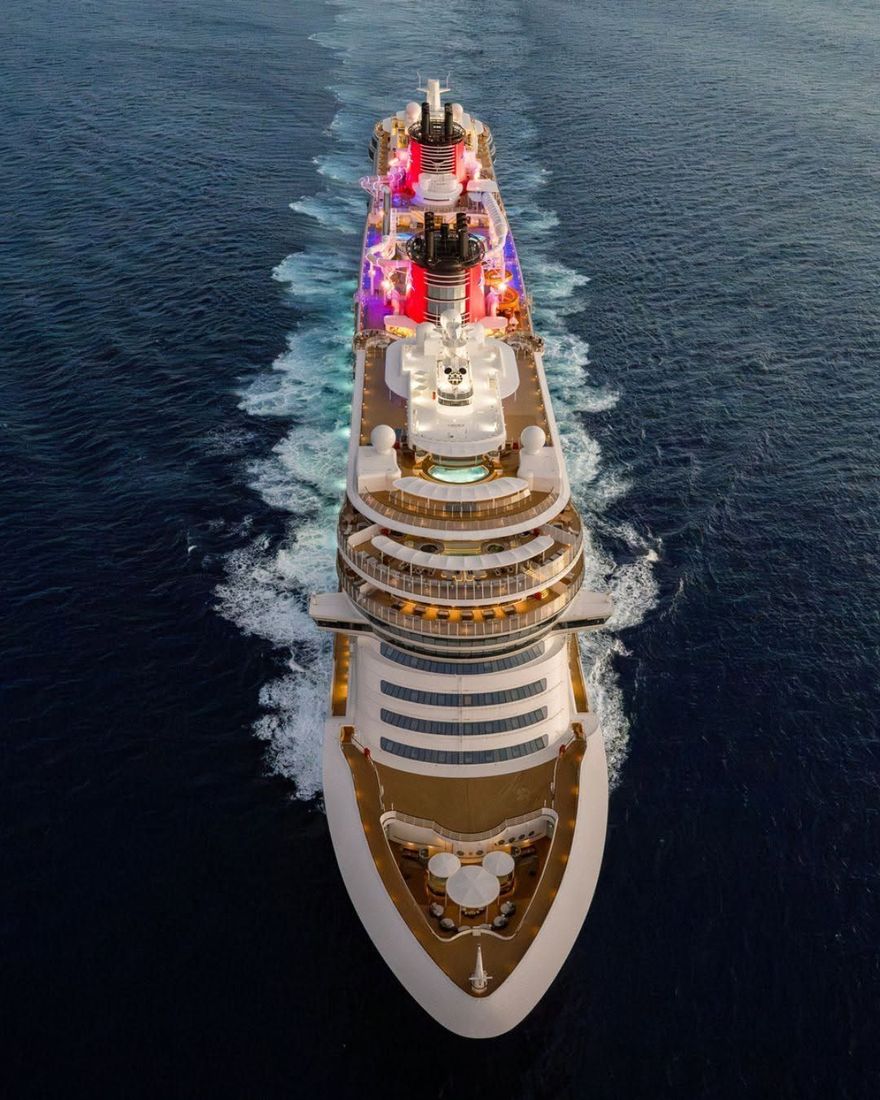 A luxury cruise ship sailing on deep blue ocean, with bright pink and white deck lights.