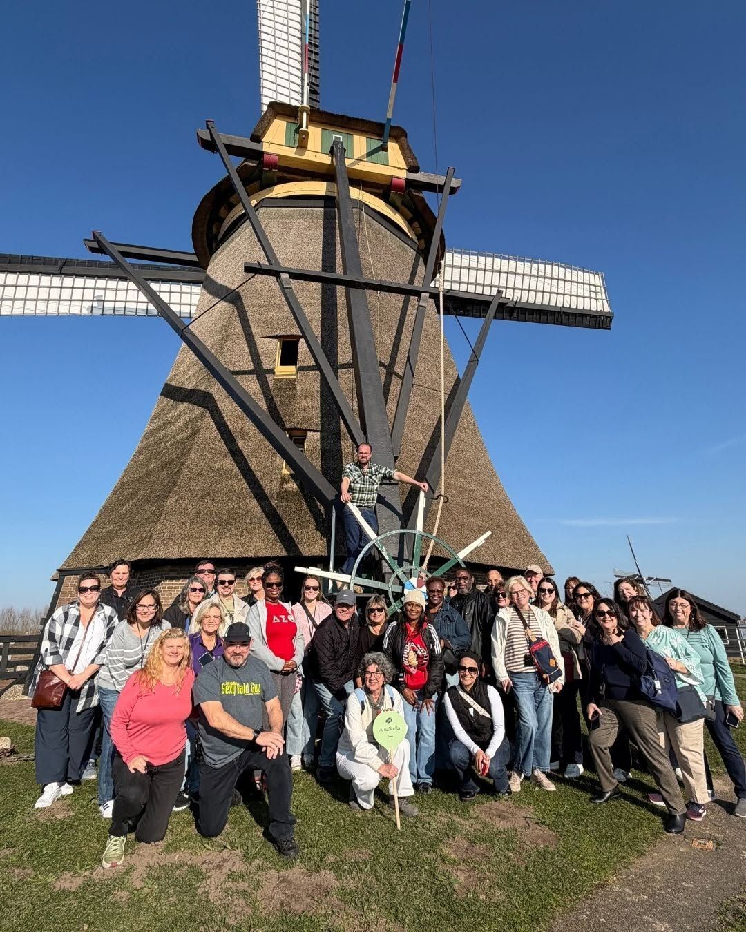 Group posing in front of a traditional windmill on a sunny day