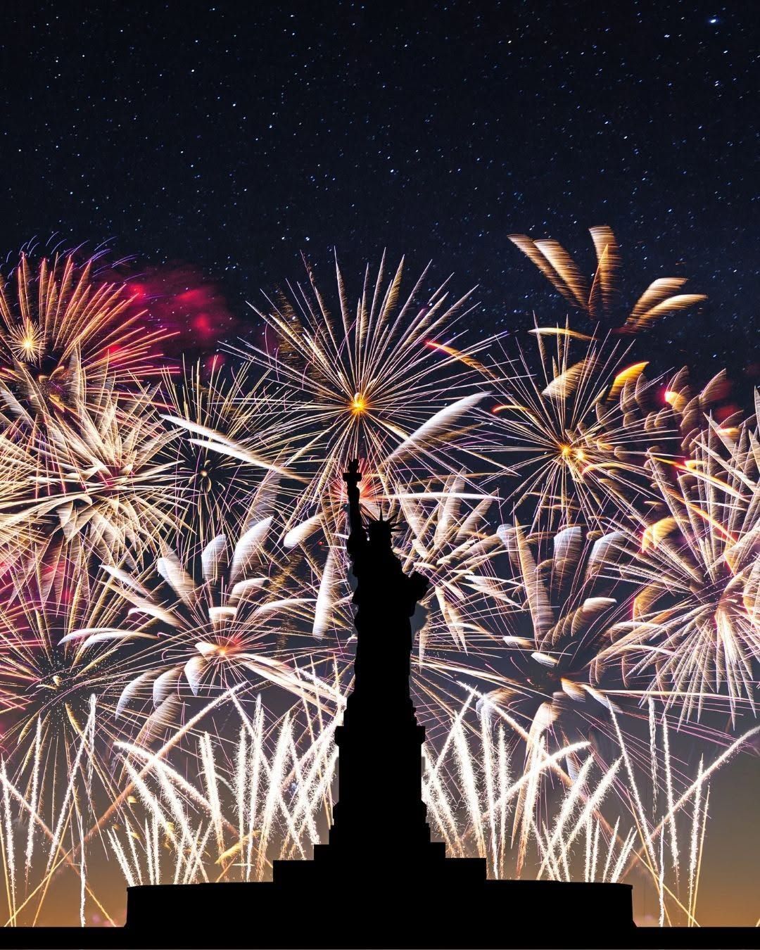 Fireworks burst behind the Statue of Liberty at night.