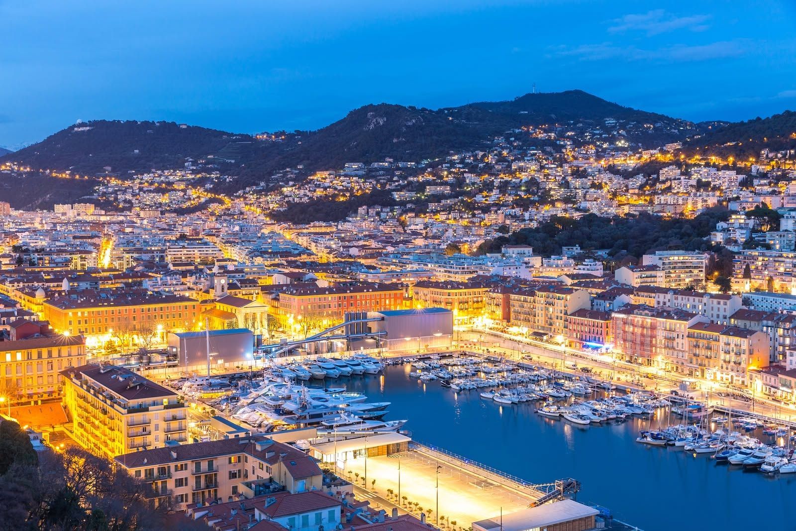 Dusk view of a brightly lit coastal city and harbor beneath dark hills