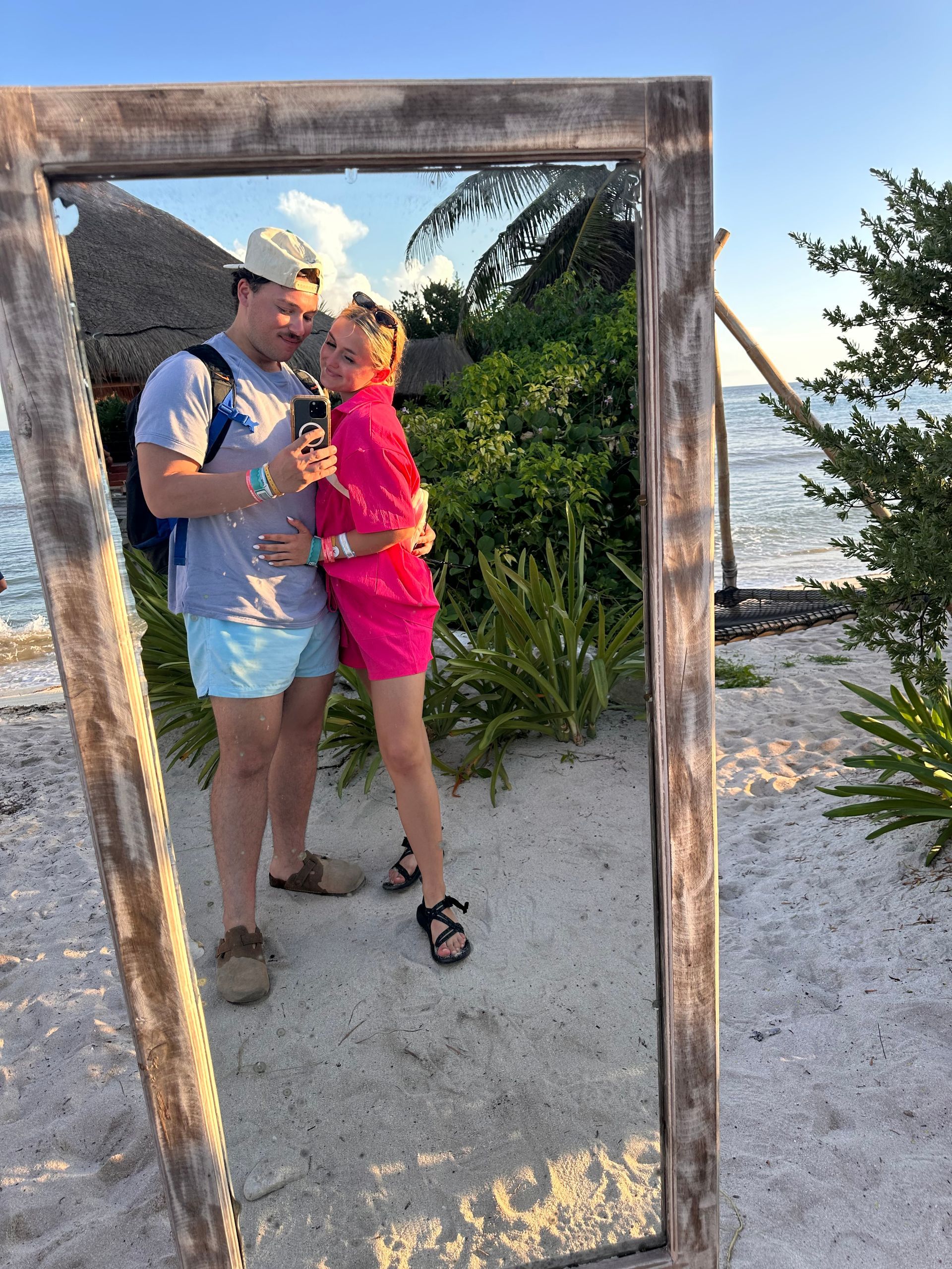Couple posing on a beach, reflected in a rustic wooden frame at sunset.