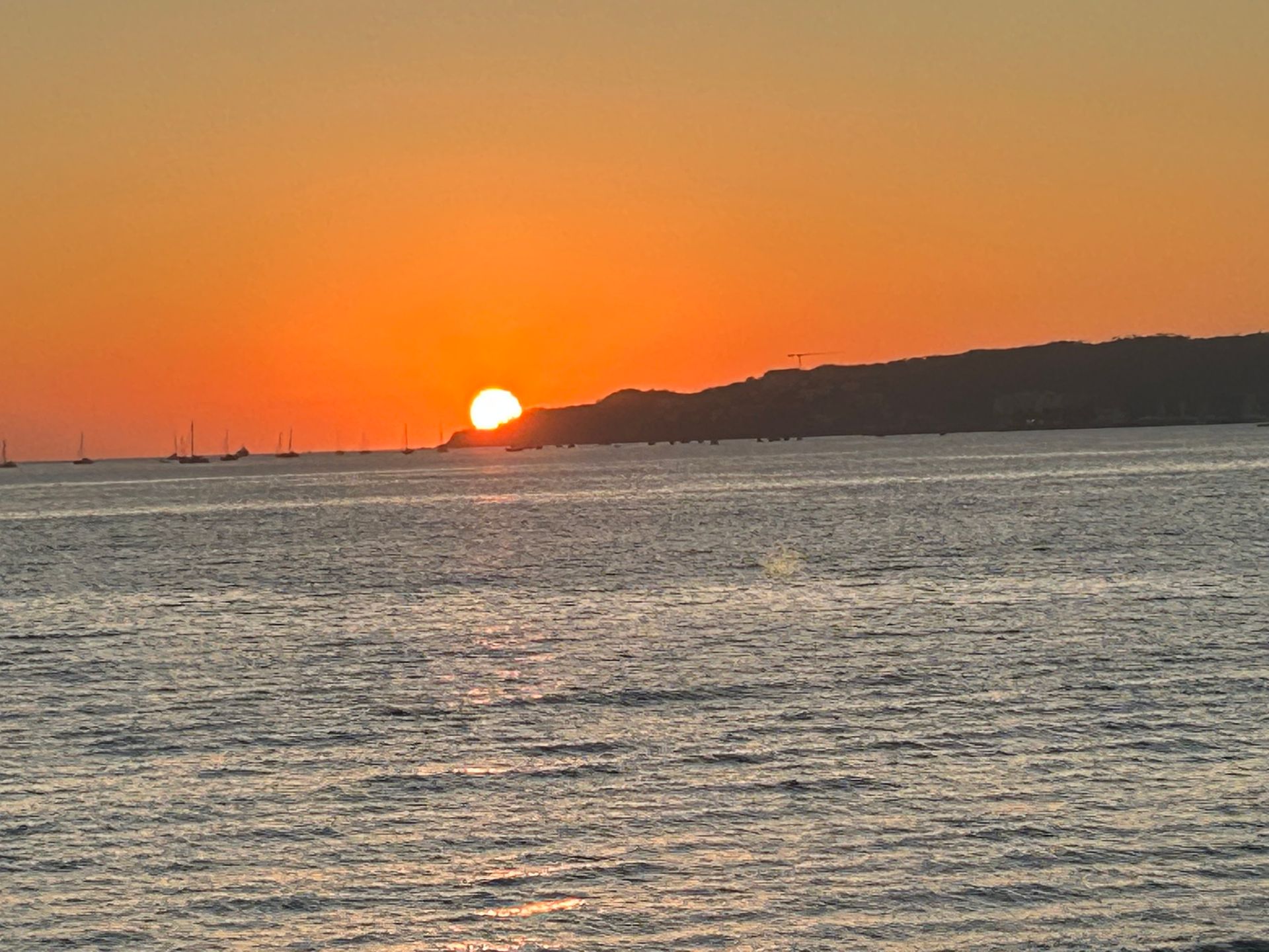 Sunset over calm ocean with orange sky and silhouetted distant shoreline