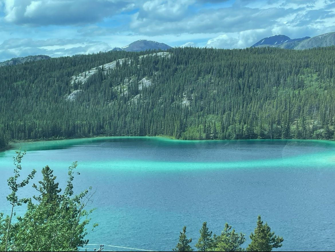 Turquoise mountain lake with forested hills and rocky peaks under a blue sky