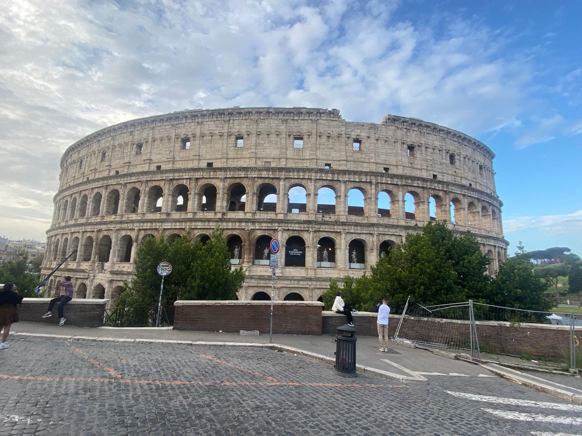 The Colosseum in Rome under a partly cloudy sky, with a few people walking in front.