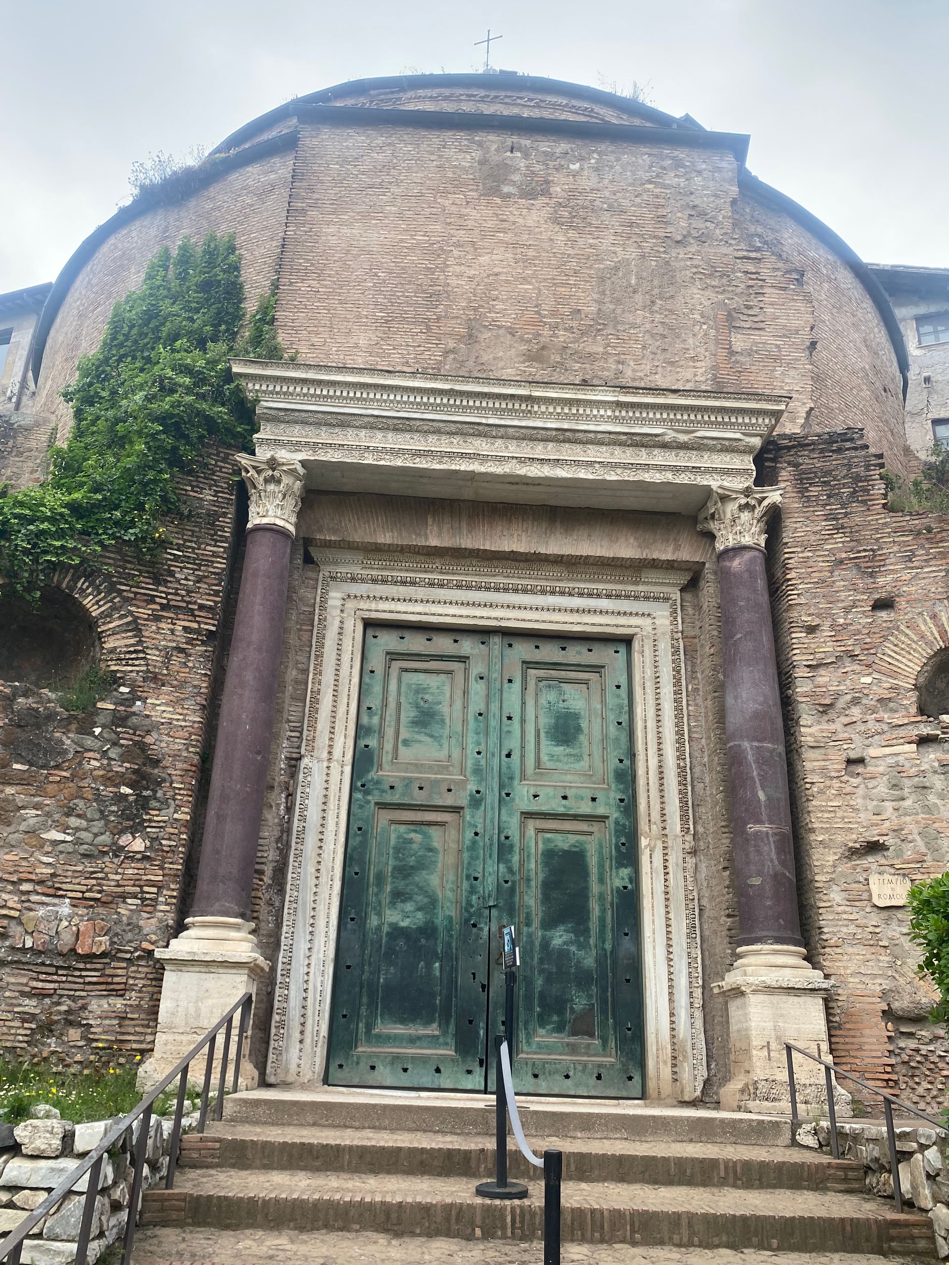 Old stone church entrance with green double doors and steps under a weathered arched facade