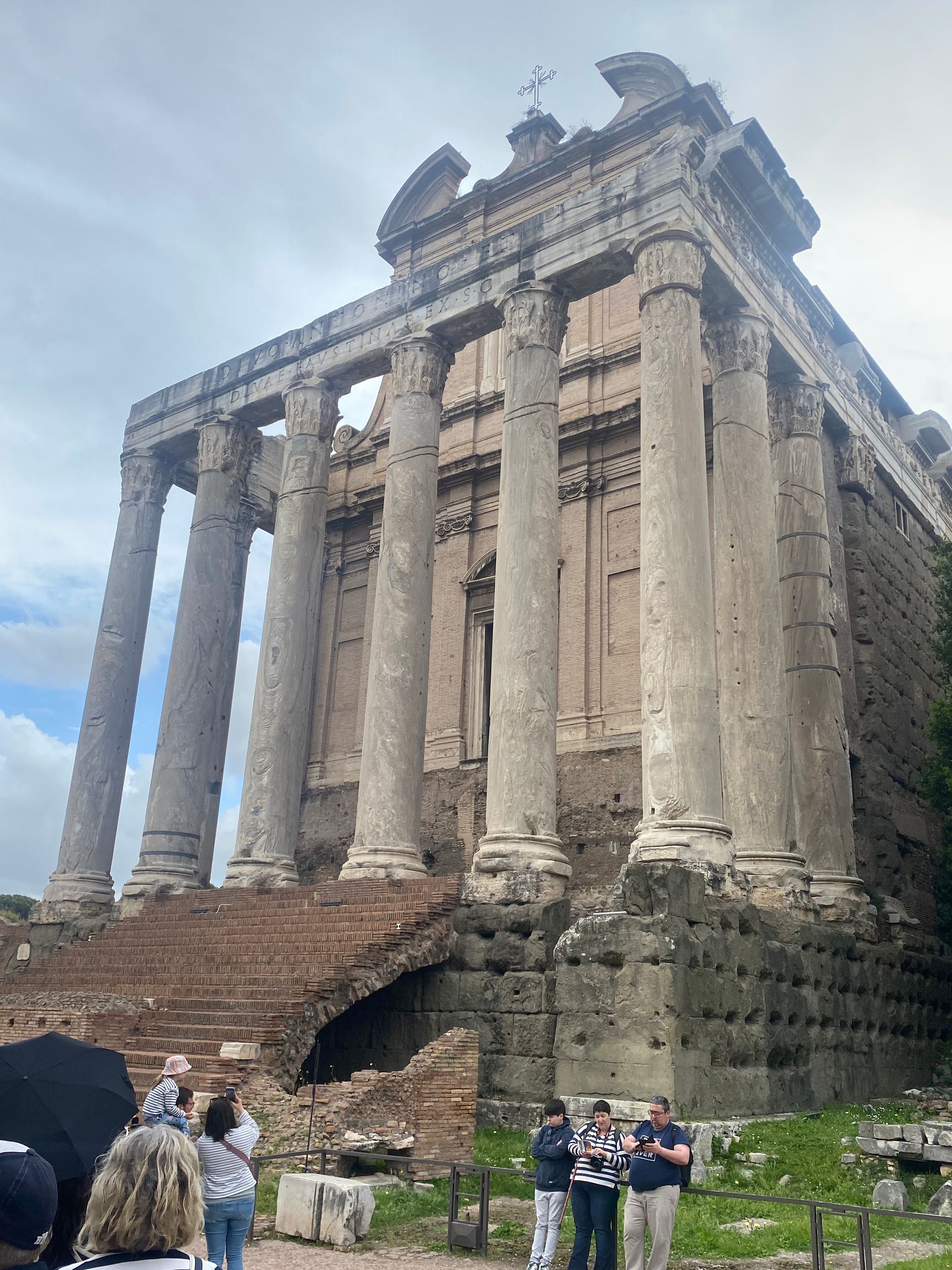 Ancient stone temple with tall columns and stairs, seen from below, with tourists at the base