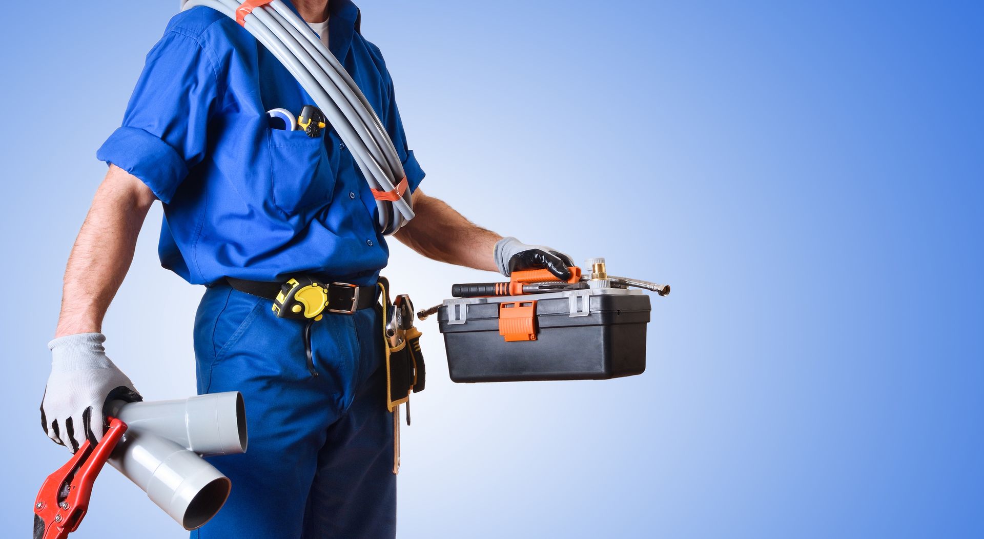 Plumber in blue uniform holding a toolbox and pipes, standing against a blue backdrop.
