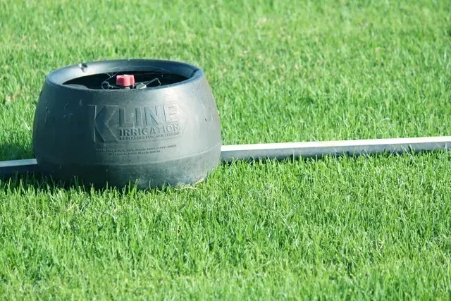 Black Metal Bin on Green Grass, with A Hose Running Behind It — Edmonds Turf in Louth Park, NSW