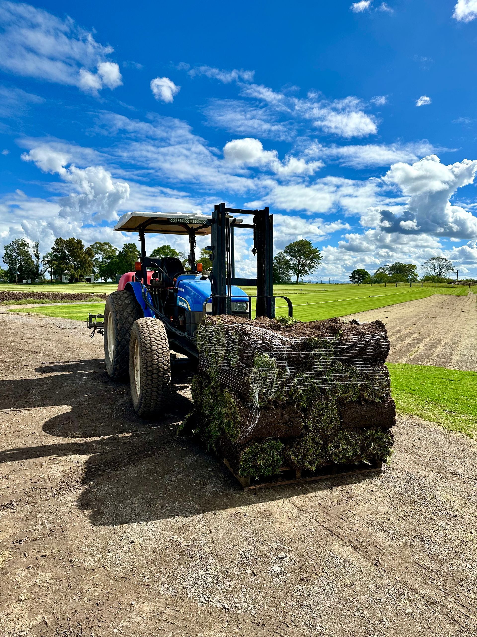 Forklift lifting a large bale of hay on a gravel farmyard under a blue sky