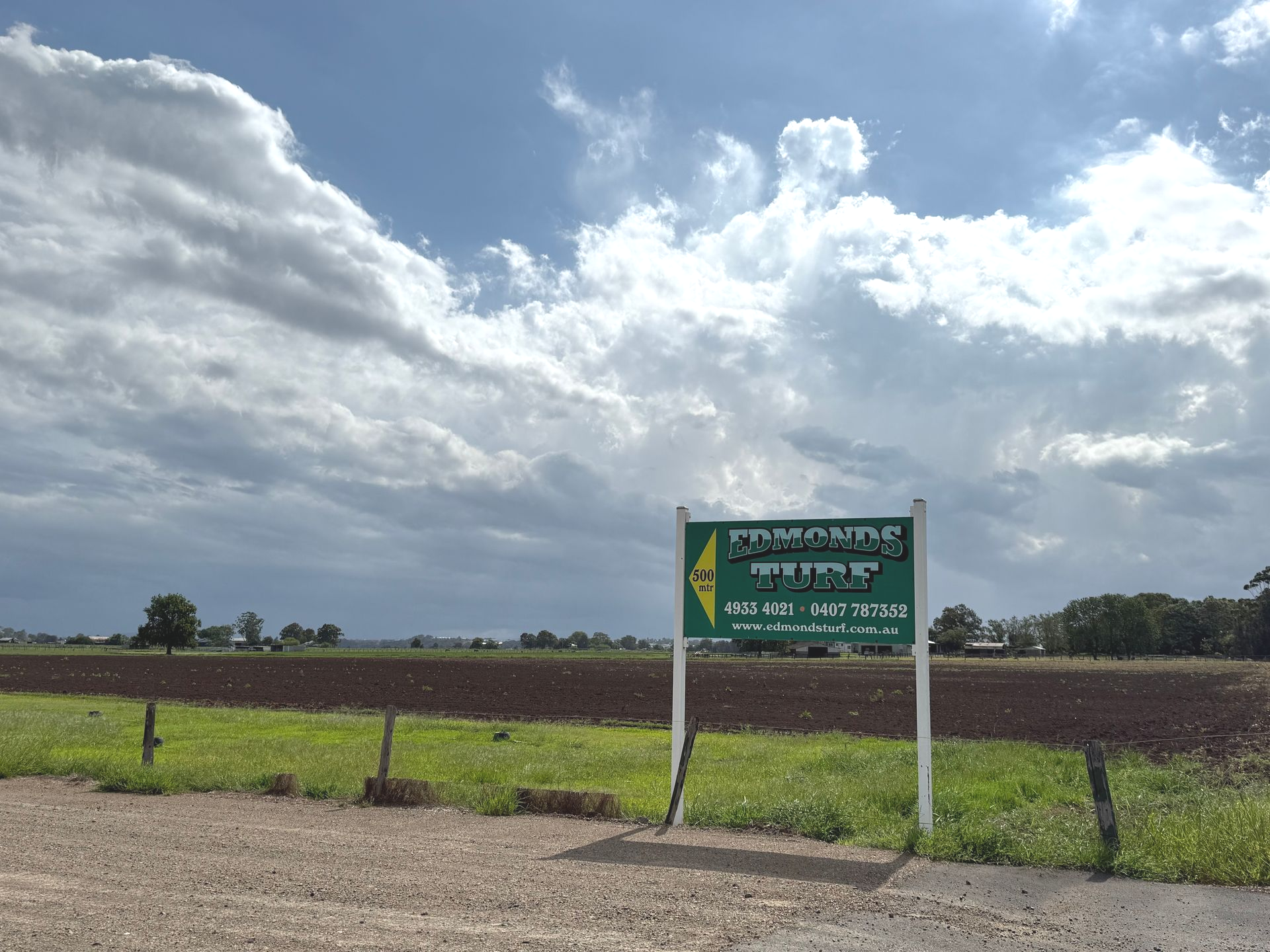 Green Roadside Sign Beside a Rural Field Under a Cloudy Sky — Edmonds Turf in Lake Macquarie, NSW