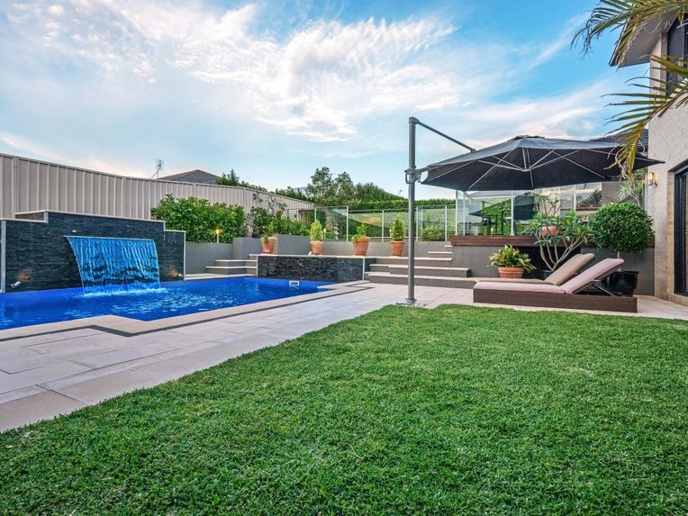 Backyard pool with blue waterfall, green lawn, and shaded lounge area — Edmonds Turf in Louth Park, NSW