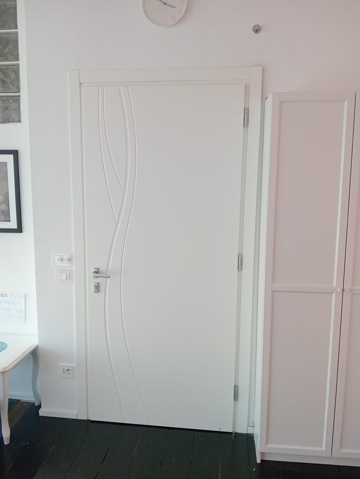 Porta in legno con ferramenta e telaio argentati, in un corridoio dalle pareti bianche, con un piccolo zerbino in basso.