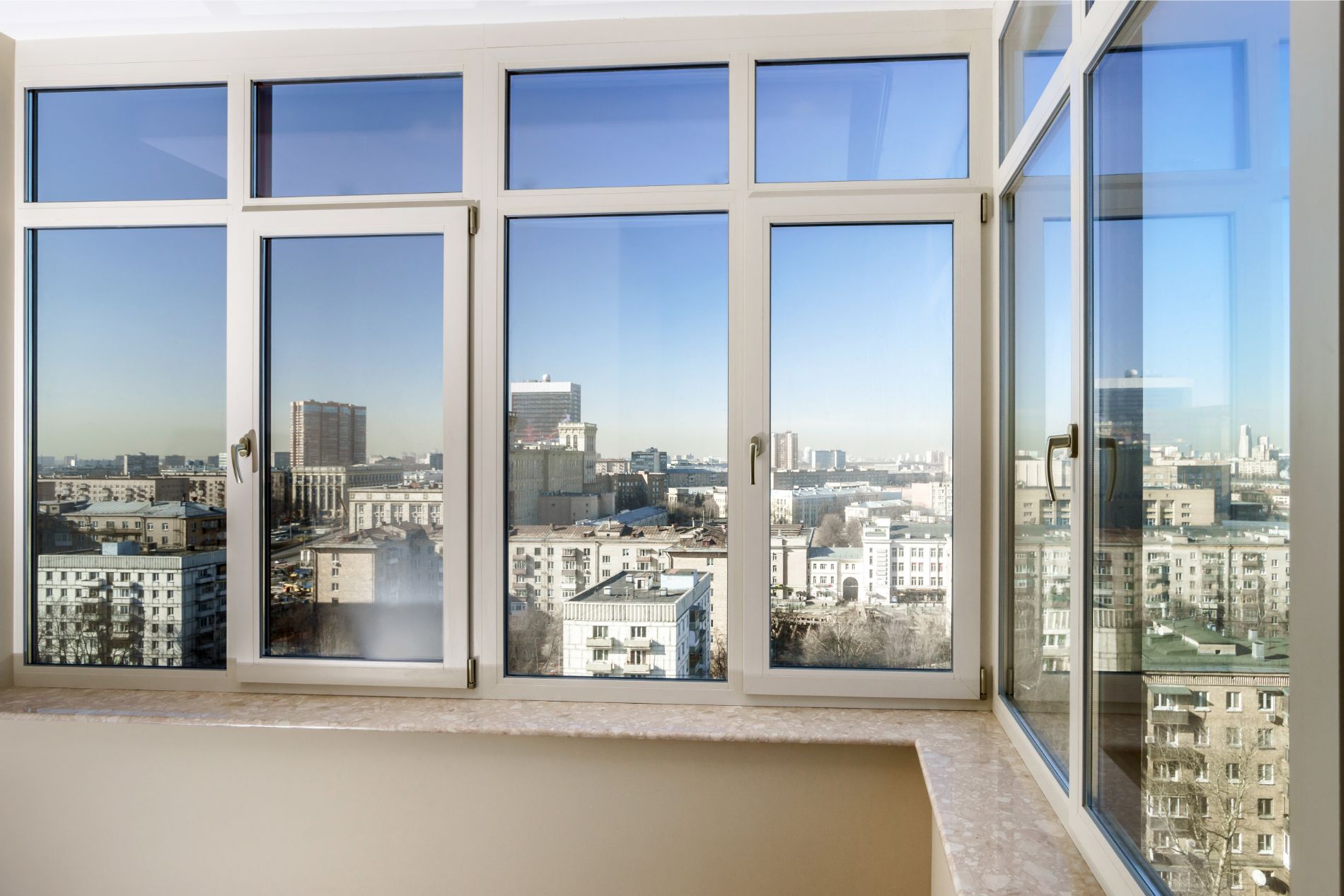 Vista della città attraverso numerose grandi finestre con cornice bianca; cielo soleggiato, edifici.