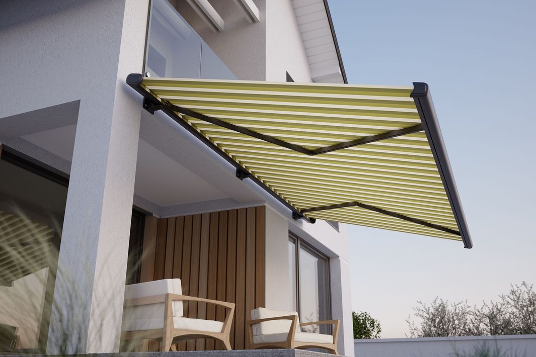 Una tenda a strisce beige e verdi si estendeva da un edificio bianco, sopra un piccolo balcone con due sedie.
