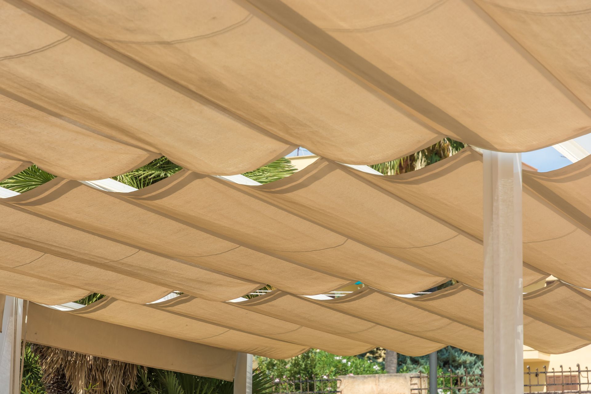 Tenda da sole retrattile beige che crea ombra, vista dal basso.