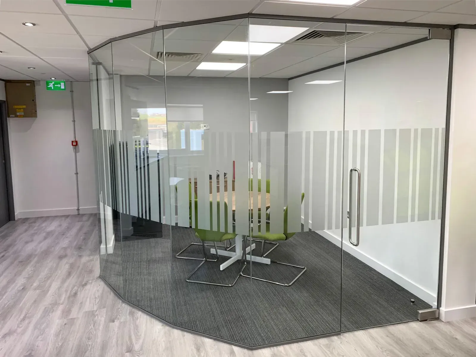Glass-walled meeting room with frosted vertical stripes. Interior view shows a table and chairs.
