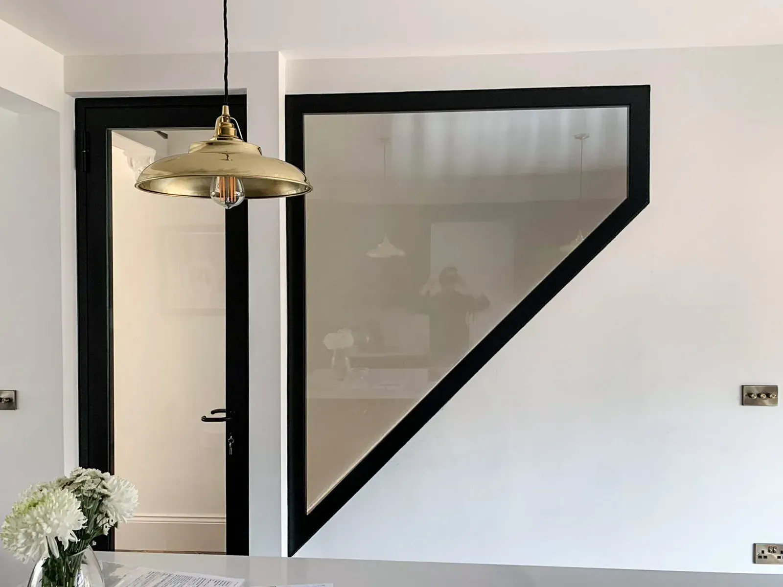 Interior with white walls, black trim, glass panel, gold pendant light, and door.