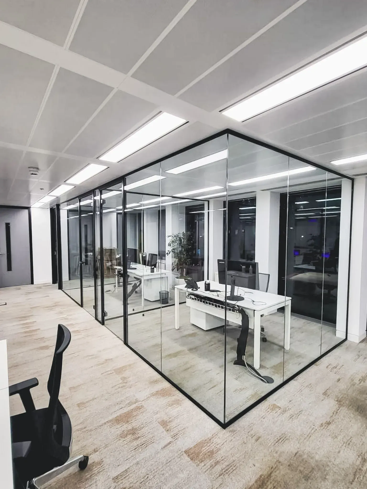 Modern office space with glass-walled rooms, white desks, and carpeted floors.