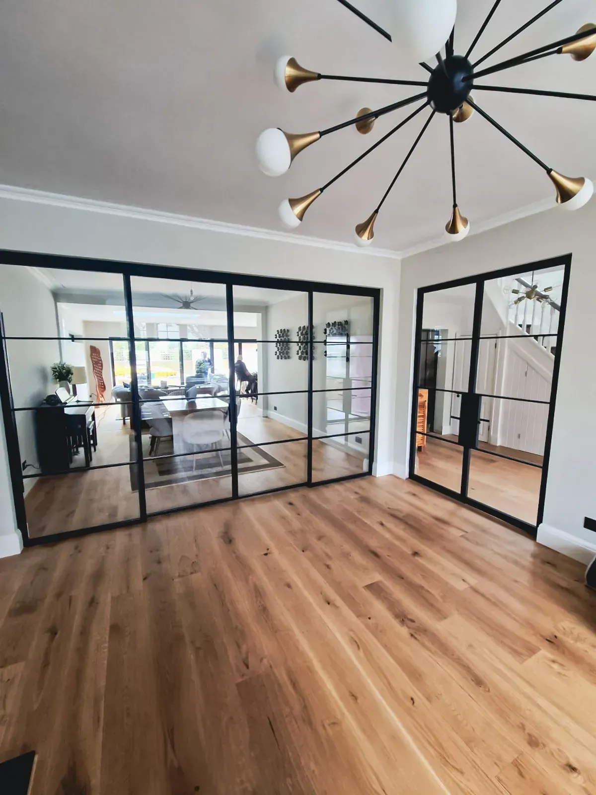 Interior room with large black-framed glass doors, hardwood floor, and a modern chandelier.