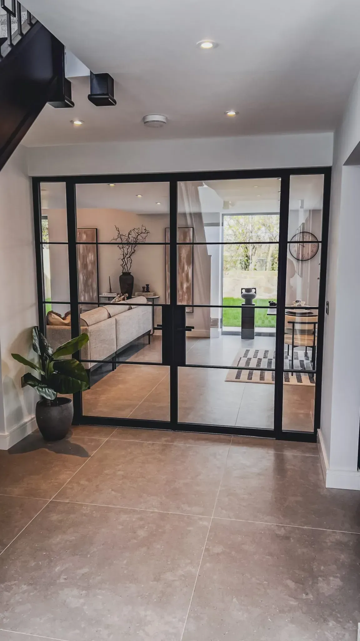 Interior view: steel-framed glass doors open to a living space with a sofa and outdoor view; gray stone flooring.