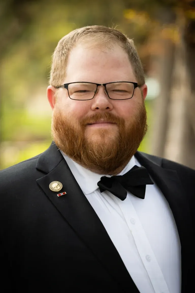 Man with glasses and a beard wearing a tuxedo with a bow tie, smiling.