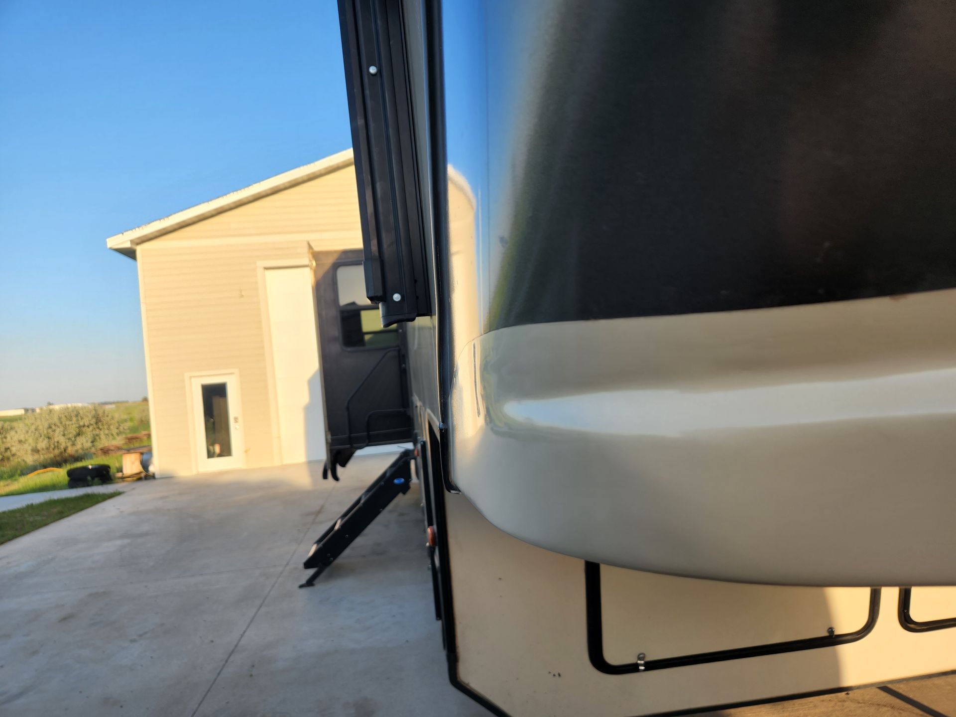 RV parked beside a beige building on a concrete driveway under a clear blue sky