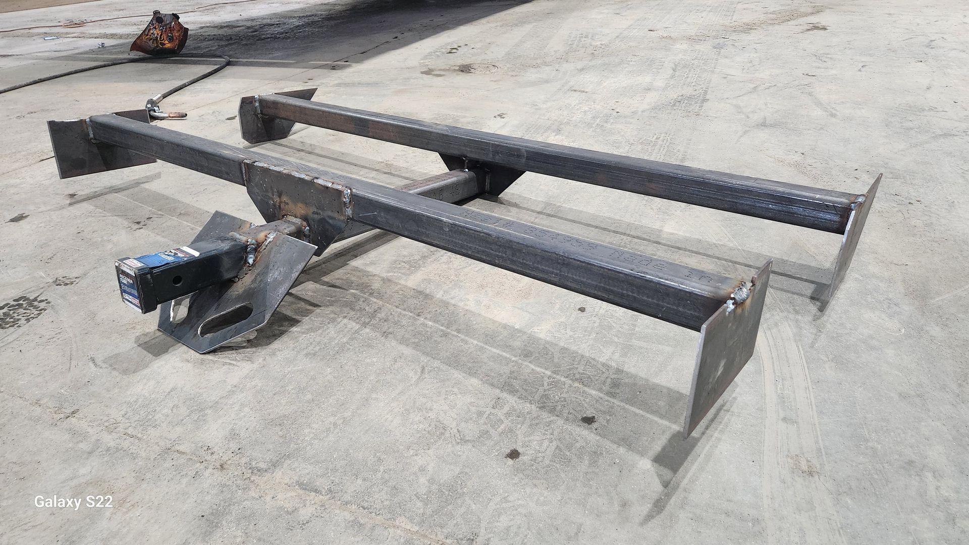 Metal frame with black beams and a small blue winch on a concrete road surface