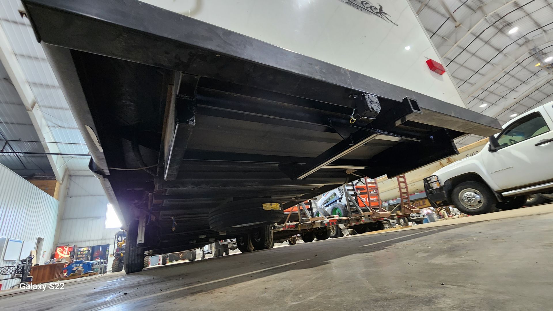 Low-angle view under a large white truck at an indoor auto show, with other vehicles in the background