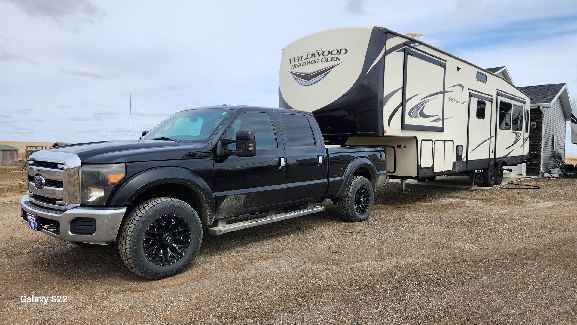 Black pickup truck towing a white RV trailer on a gravel lot under a cloudy sky