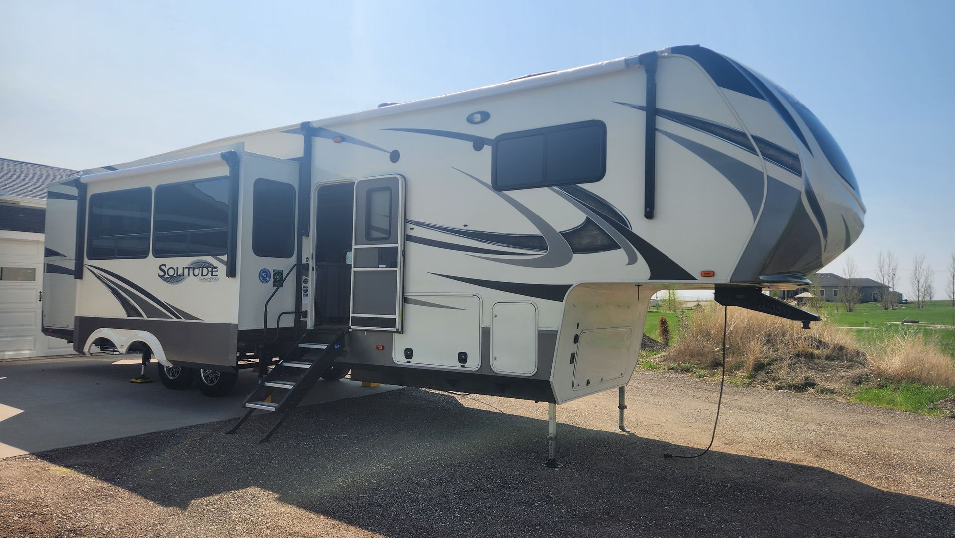 White fifth-wheel RV camper parked on gravel in a sunny, open lot