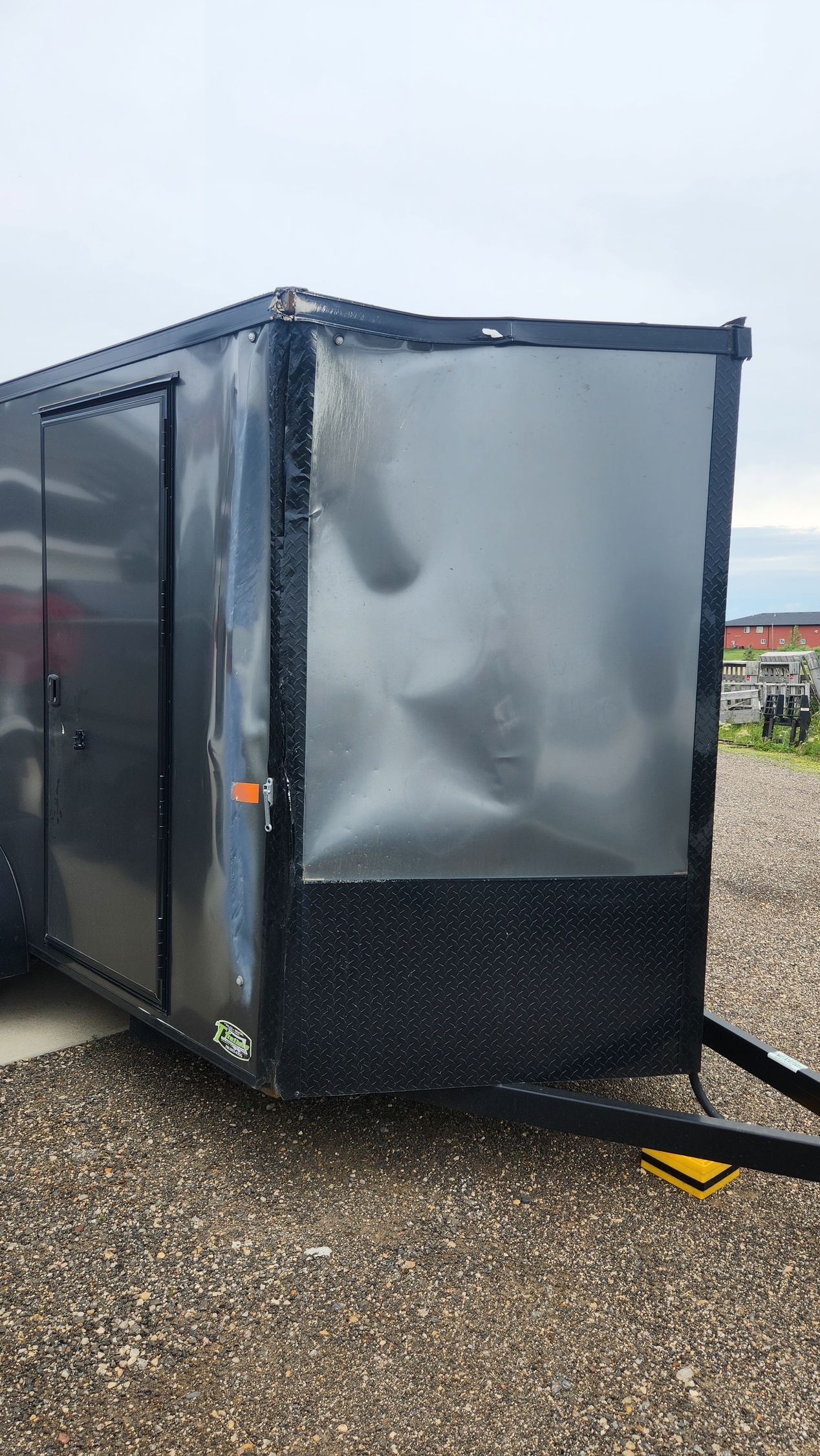 Black enclosed utility trailer with a dented silver front panel on a gravel lot