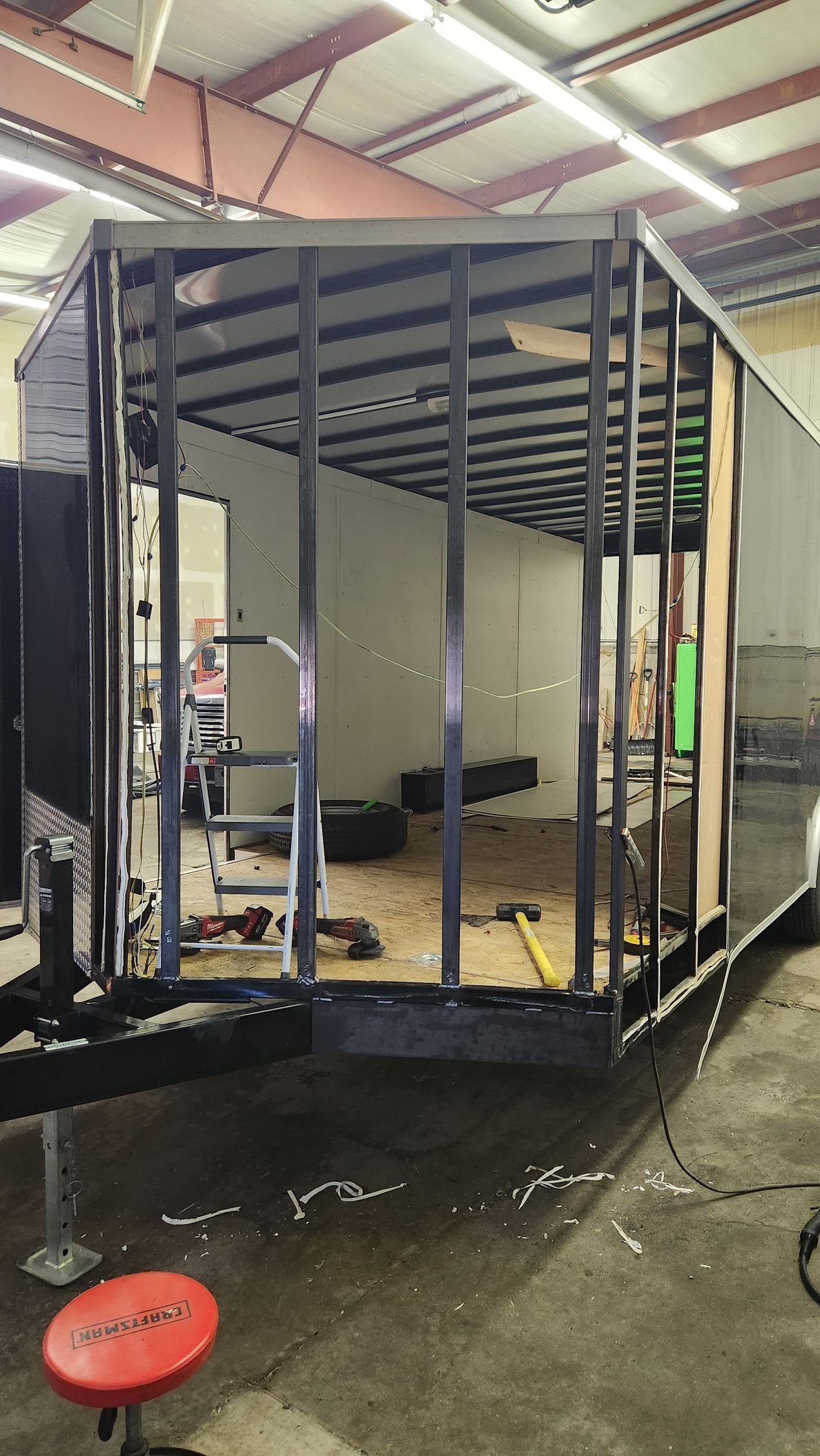 Partially built trailer frame indoors with exposed metal studs and a white exterior panel.