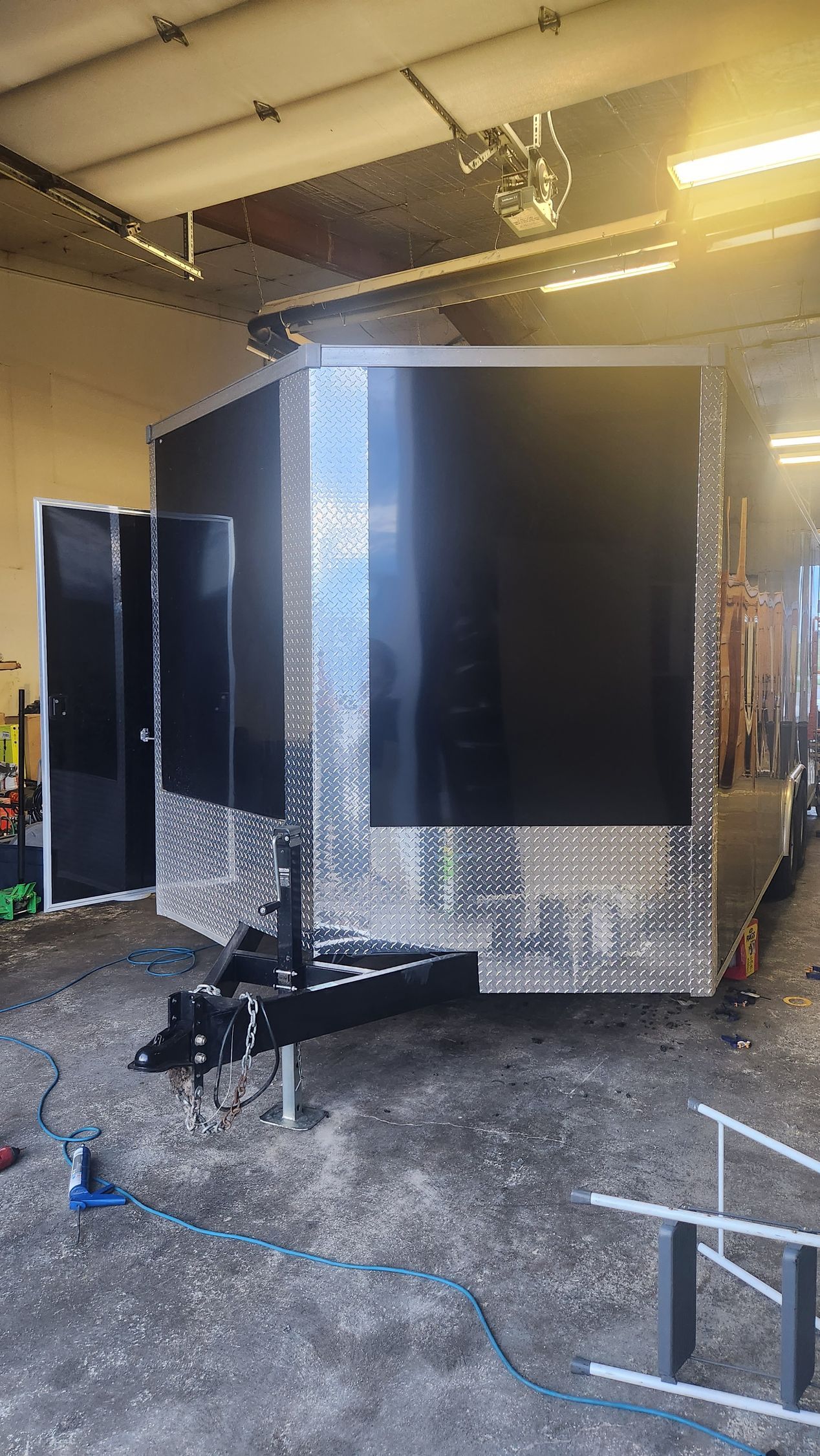 Large black-and-silver trailer or equipment enclosure in a warehouse, with wheels and a ladder nearby.